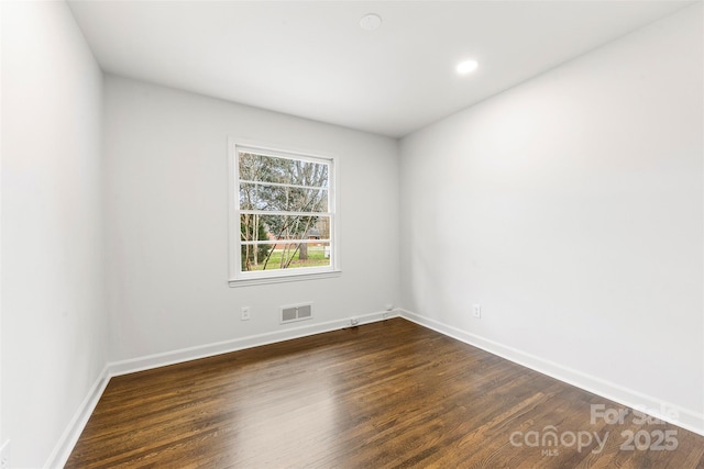 unfurnished room with dark wood-type flooring, visible vents, and baseboards