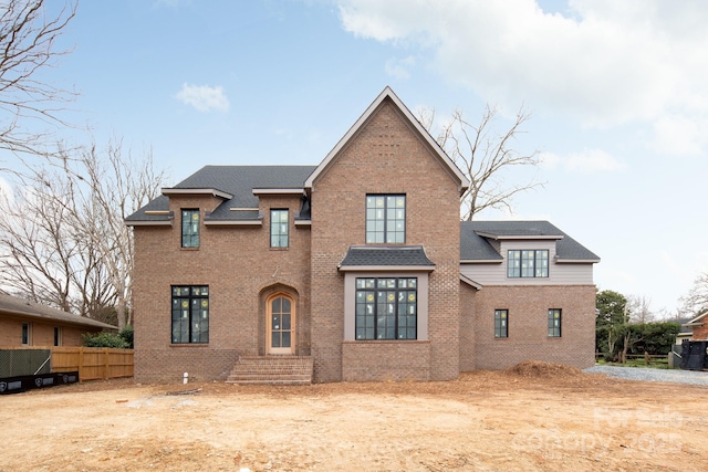 traditional-style home with roof with shingles, fence, and brick siding