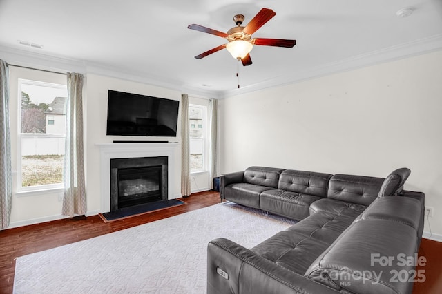 living room with wood finished floors, visible vents, a fireplace with flush hearth, ceiling fan, and ornamental molding