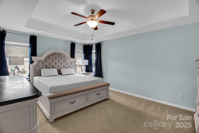 bedroom with a tray ceiling, multiple windows, baseboards, and light carpet