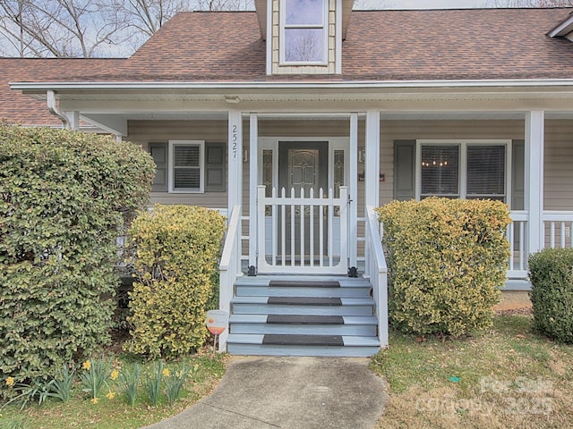 entrance to property with a porch and roof with shingles