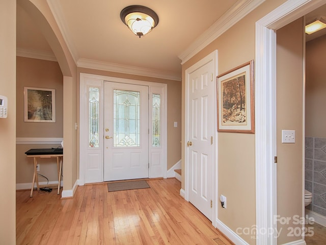 foyer entrance featuring ornamental molding, arched walkways, light wood-style flooring, and baseboards