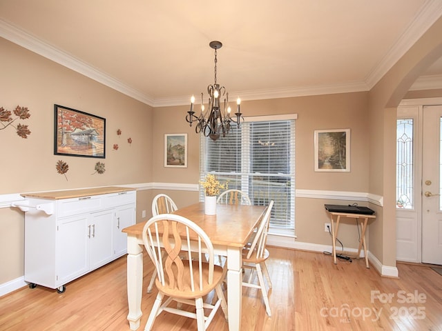 dining space featuring light wood-type flooring, baseboards, arched walkways, and ornamental molding