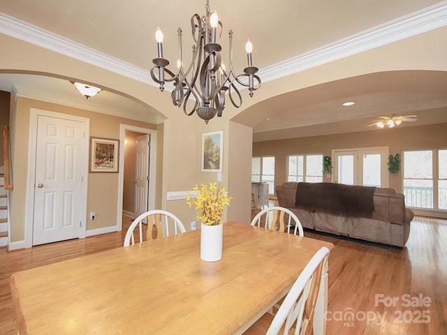 dining space with arched walkways, baseboards, light wood-style flooring, ceiling fan, and crown molding