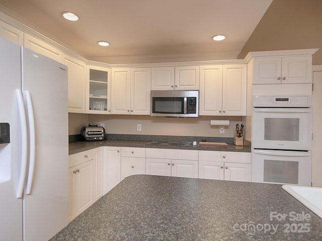 kitchen with dark countertops, white appliances, and white cabinetry