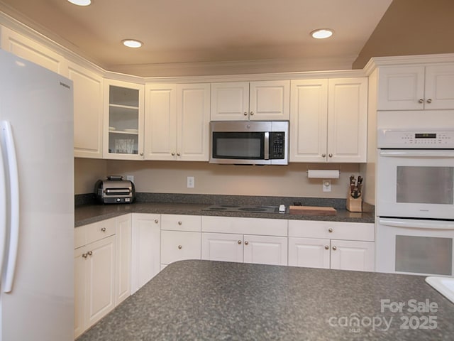 kitchen with white appliances, dark countertops, glass insert cabinets, and white cabinets