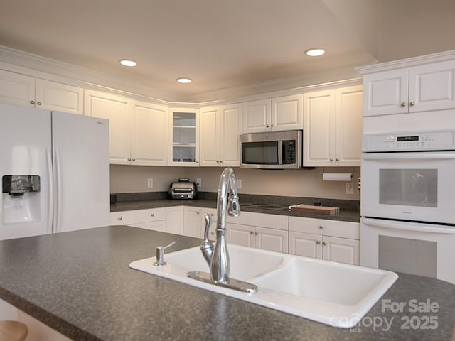 kitchen featuring white appliances, dark countertops, glass insert cabinets, white cabinetry, and recessed lighting