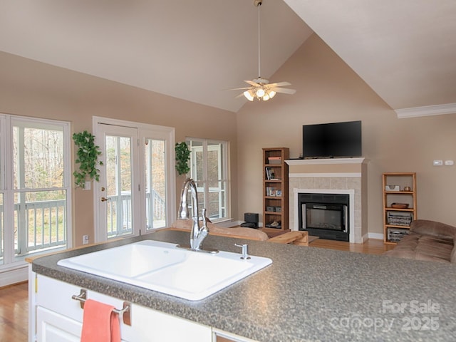 kitchen with ceiling fan, a sink, white cabinetry, light wood-type flooring, and a tiled fireplace