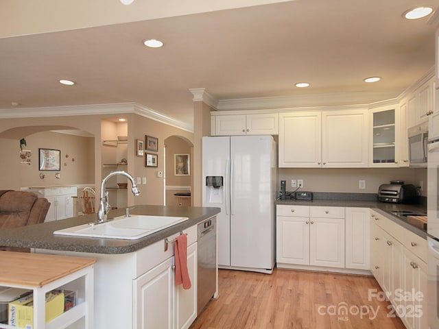 kitchen with arched walkways, dark countertops, light wood-style floors, a sink, and white appliances