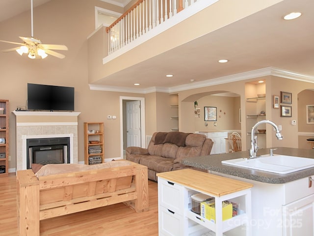 living area with ceiling fan, arched walkways, a tile fireplace, light wood-style floors, and crown molding