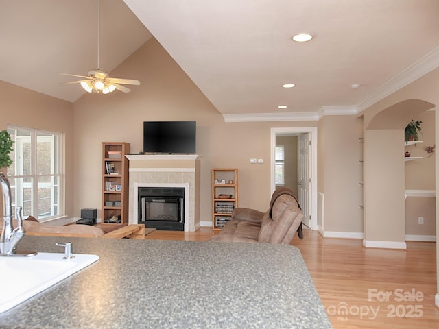 living room featuring baseboards, arched walkways, a tile fireplace, light wood-style flooring, and crown molding