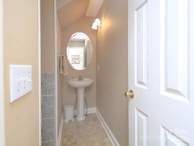 bathroom with vaulted ceiling, a sink, tile patterned floors, and baseboards