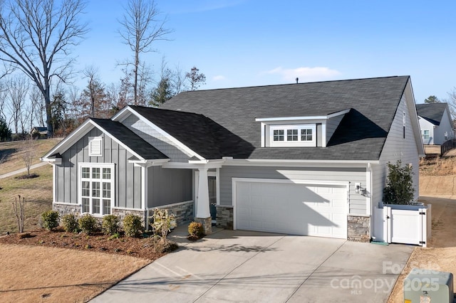 craftsman house with driveway, a gate, stone siding, fence, and board and batten siding