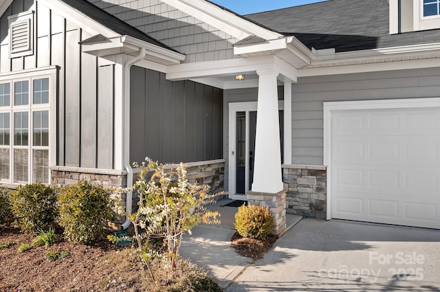 property entrance with stone siding, board and batten siding, a garage, and roof with shingles