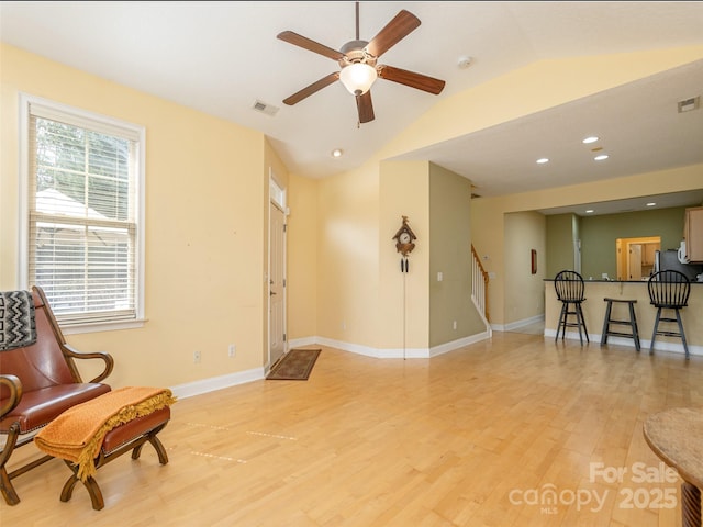 sitting room featuring visible vents, baseboards, light wood-style flooring, stairs, and vaulted ceiling