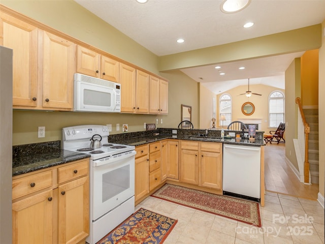 kitchen featuring lofted ceiling, light brown cabinets, dark stone countertops, white appliances, and a peninsula