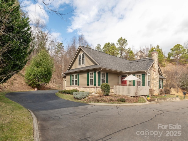 view of side of property with driveway, stone siding, a chimney, and roof with shingles