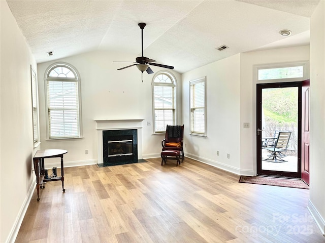 living area with a fireplace with flush hearth, vaulted ceiling, a ceiling fan, light wood-type flooring, and a textured ceiling