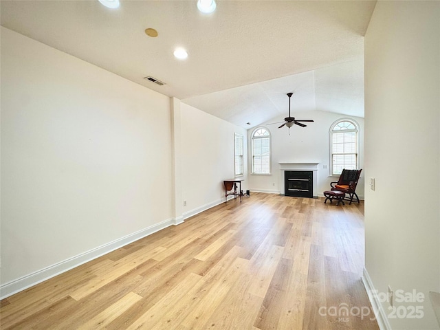 unfurnished living room with vaulted ceiling, visible vents, a ceiling fan, light wood-type flooring, and a fireplace