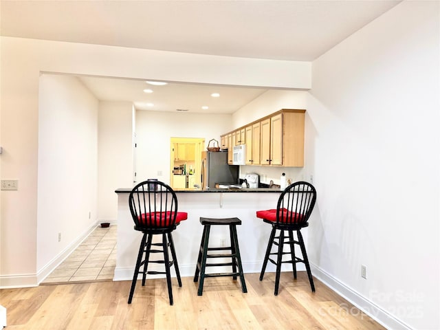 kitchen featuring a breakfast bar, freestanding refrigerator, white microwave, a peninsula, and recessed lighting