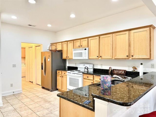 kitchen with dark stone counters, white appliances, a peninsula, washer / clothes dryer, and visible vents