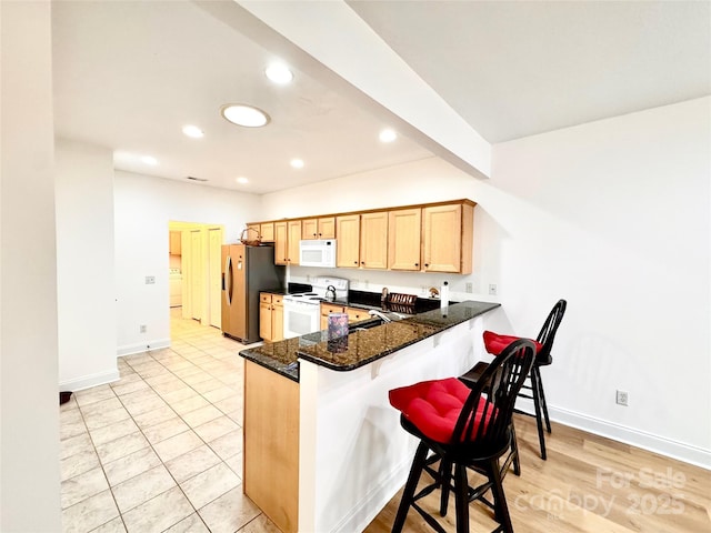 kitchen featuring a peninsula, baseboards, recessed lighting, white appliances, and a breakfast bar area