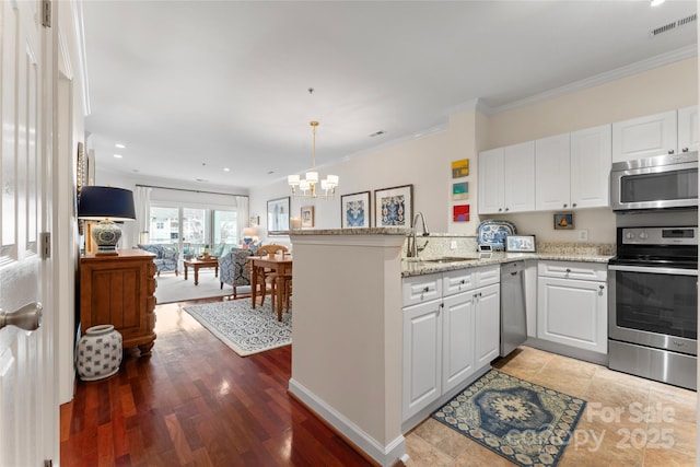 kitchen featuring a sink, appliances with stainless steel finishes, a peninsula, visible vents, and an inviting chandelier