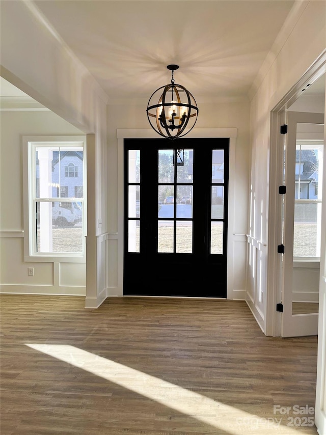 entryway with a notable chandelier, plenty of natural light, wood finished floors, and crown molding