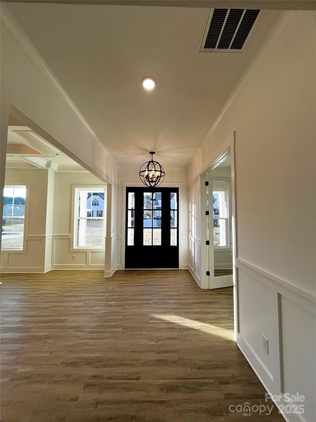 foyer entrance with visible vents, wood finished floors, crown molding, a decorative wall, and a notable chandelier