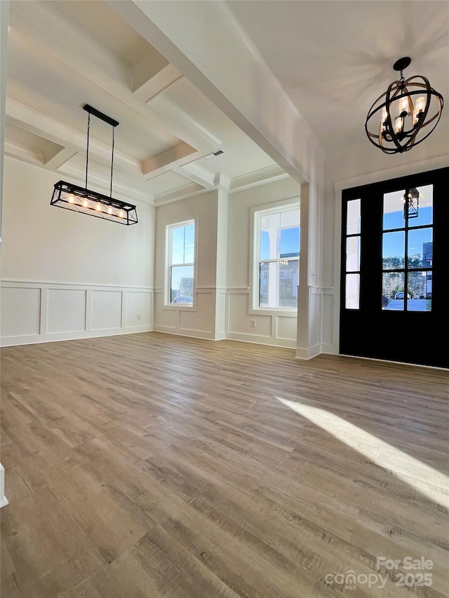 entryway featuring beam ceiling, a notable chandelier, a decorative wall, wood finished floors, and coffered ceiling