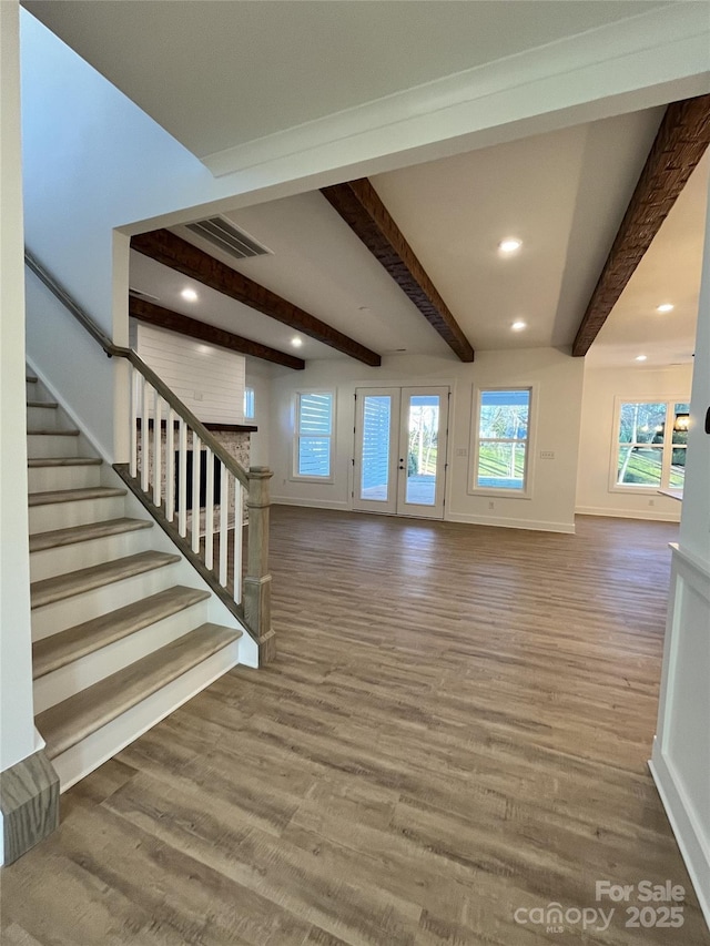 unfurnished living room with stairs, beamed ceiling, and wood finished floors