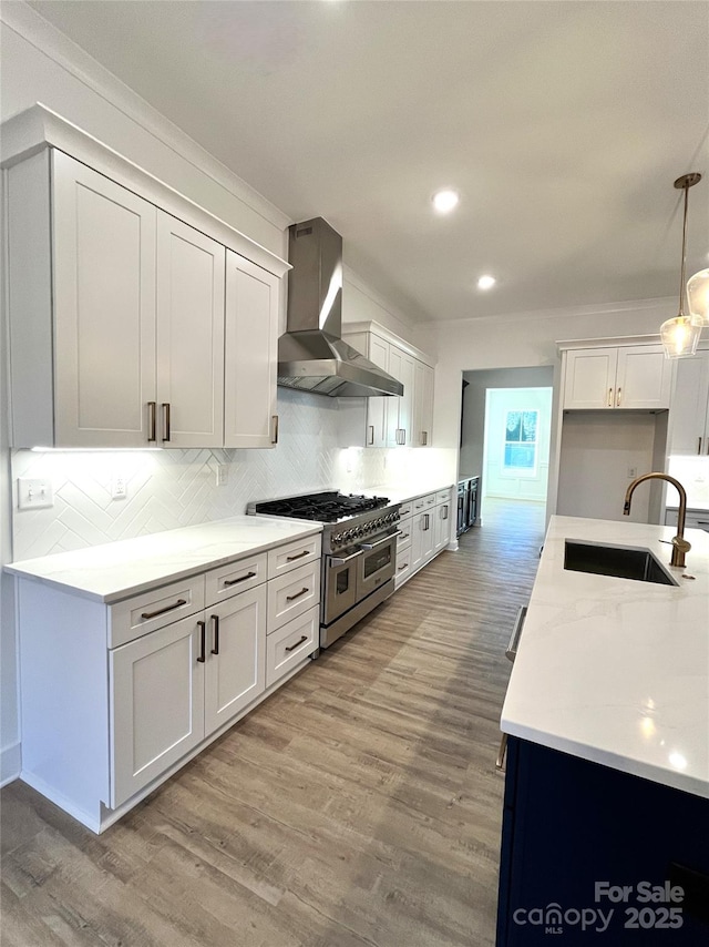 kitchen with range with two ovens, light wood-style floors, a sink, wall chimney range hood, and backsplash