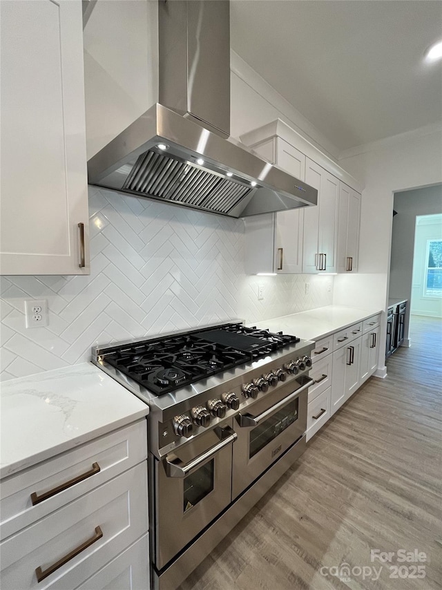 kitchen featuring light wood finished floors, range with two ovens, wall chimney range hood, white cabinetry, and backsplash