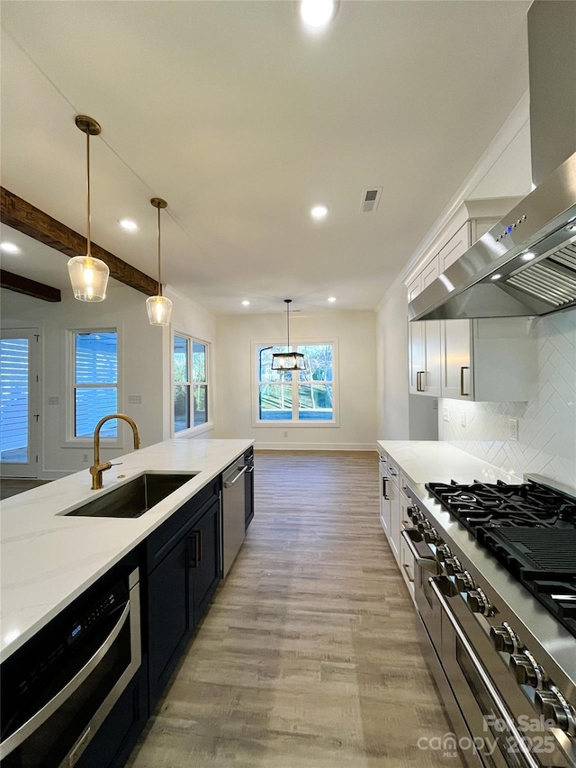 kitchen featuring visible vents, appliances with stainless steel finishes, light wood-style floors, a sink, and exhaust hood