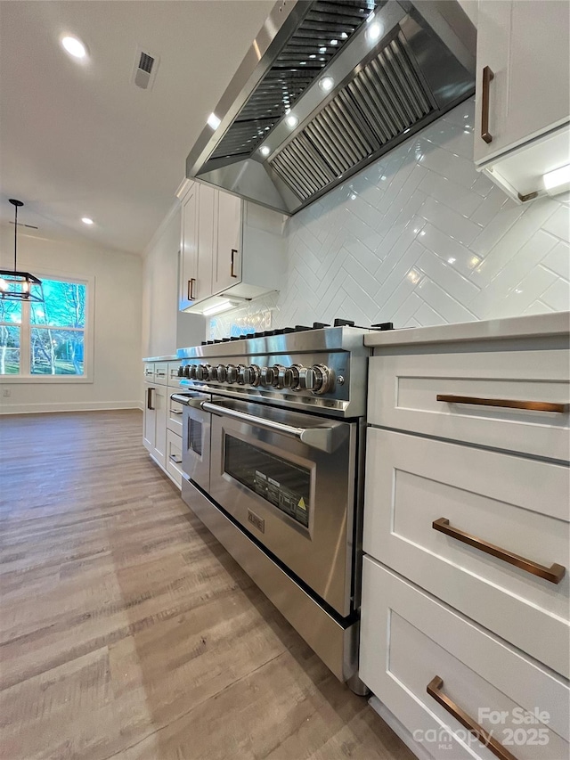 kitchen with visible vents, range with two ovens, decorative backsplash, light wood-style flooring, and custom exhaust hood