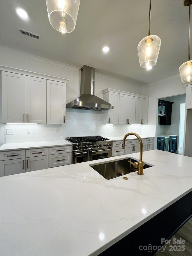 kitchen with wall chimney range hood, a sink, light stone counters, and double oven range