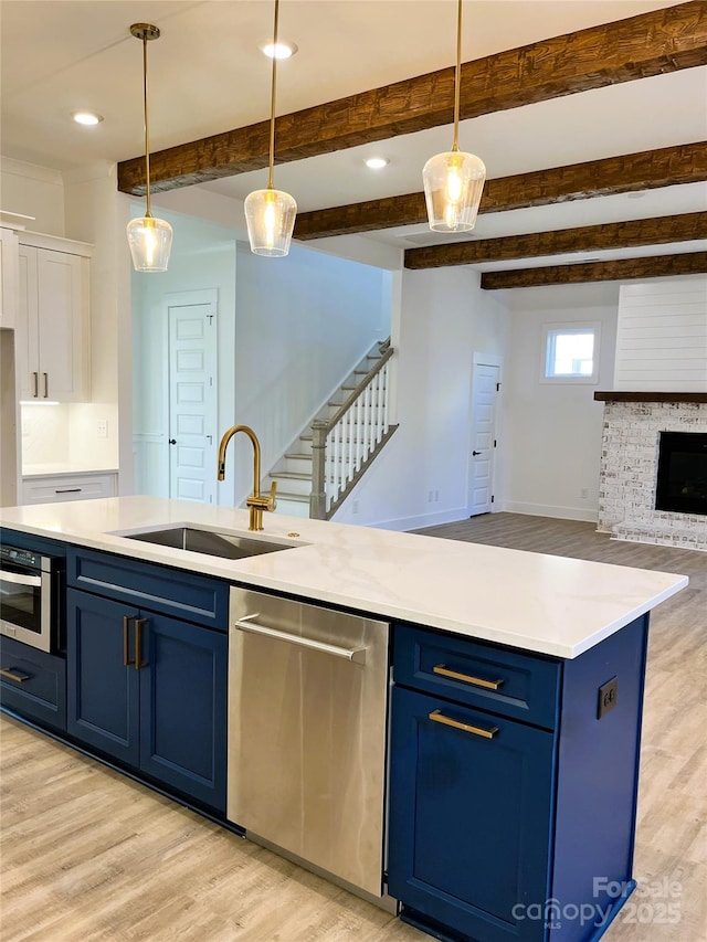 kitchen featuring light wood finished floors, appliances with stainless steel finishes, open floor plan, blue cabinetry, and a sink