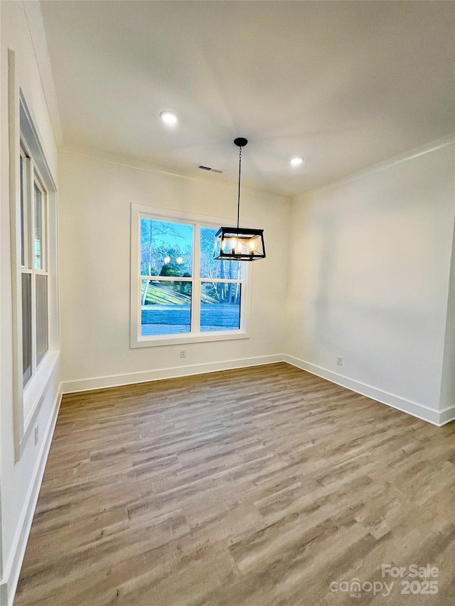 unfurnished dining area featuring an inviting chandelier, visible vents, baseboards, and wood finished floors