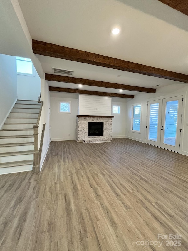 unfurnished living room featuring wood finished floors, visible vents, baseboards, stairs, and beamed ceiling