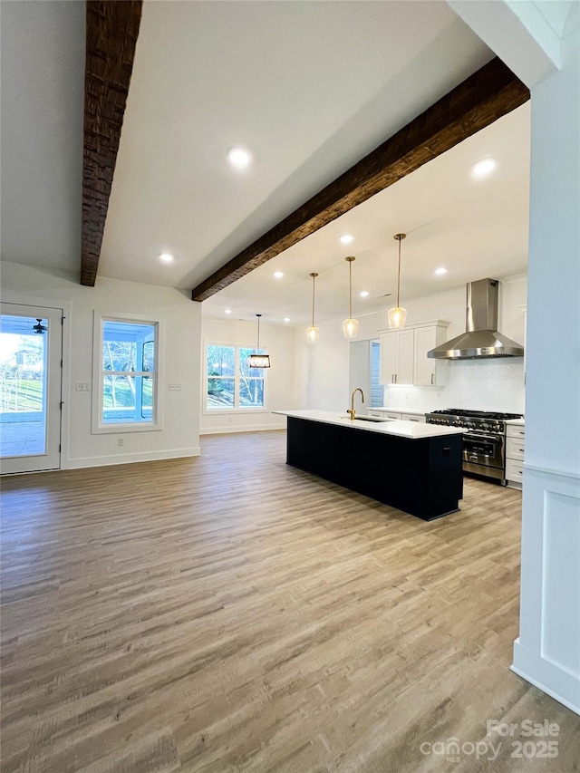 kitchen featuring light wood finished floors, high end stainless steel range, light countertops, wall chimney range hood, and an island with sink