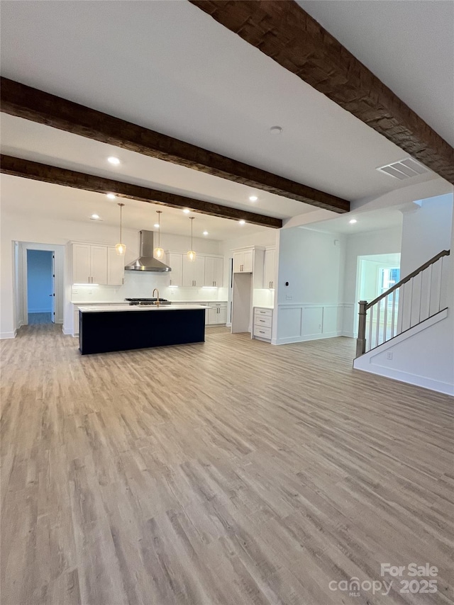 unfurnished living room featuring visible vents, beamed ceiling, stairs, and light wood-style flooring