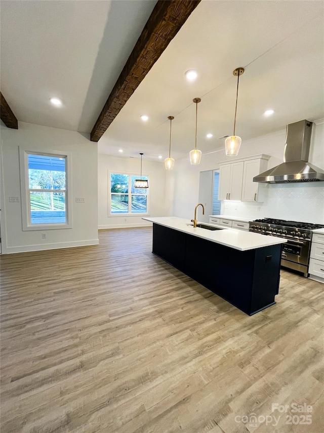 kitchen featuring wall chimney exhaust hood, beam ceiling, an island with sink, and high end range