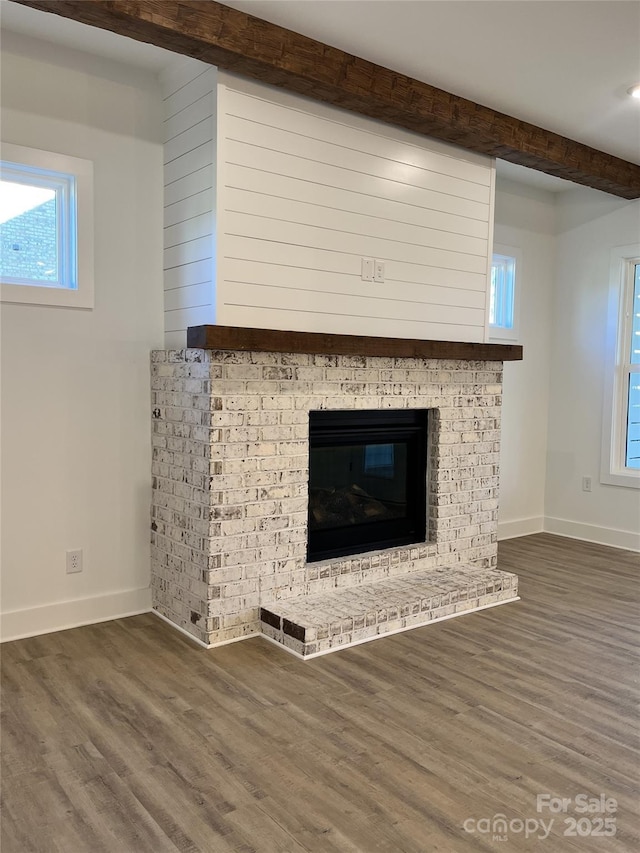 details featuring a brick fireplace, beam ceiling, baseboards, and wood finished floors