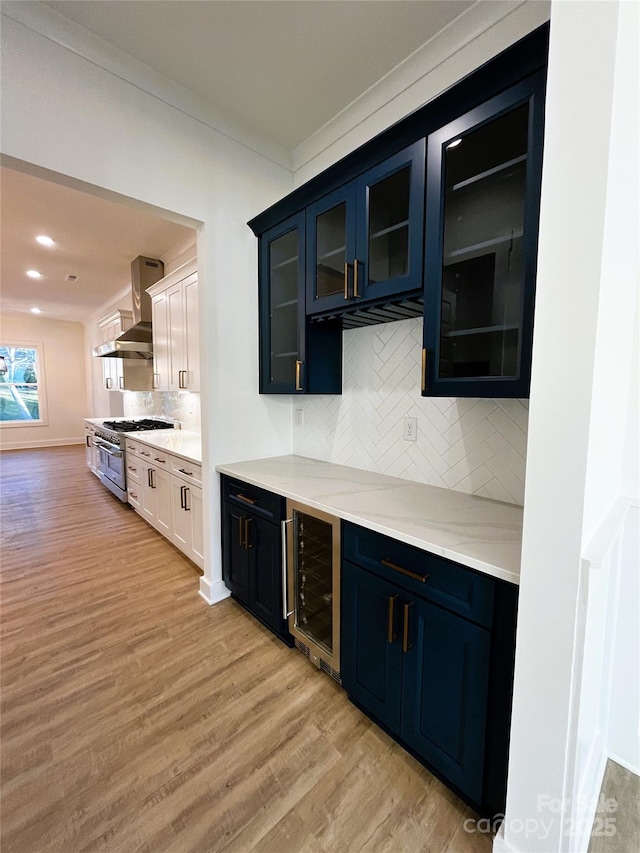 bar featuring light wood-style flooring, beverage cooler, wall chimney range hood, high end range, and tasteful backsplash