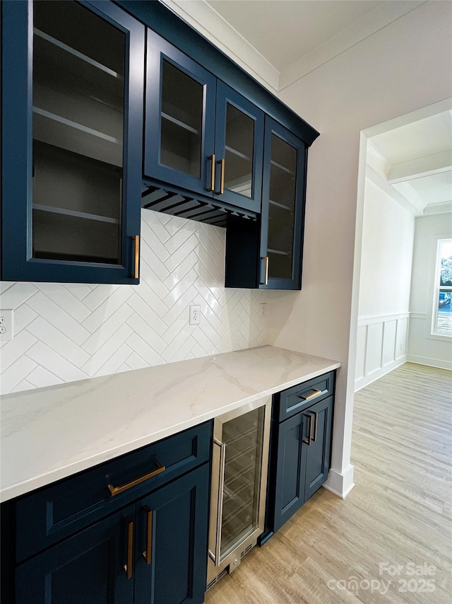 kitchen with light wood finished floors, beverage cooler, ornamental molding, light stone countertops, and backsplash