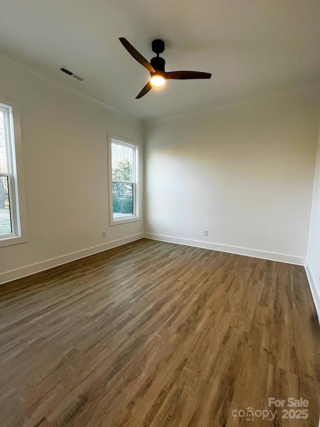 empty room with dark wood-style floors, ceiling fan, visible vents, and baseboards