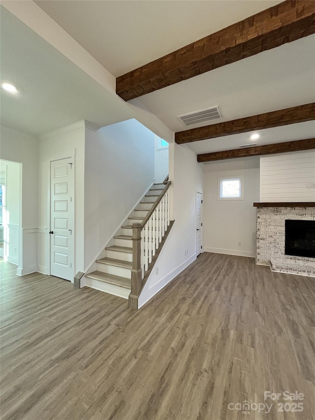 unfurnished living room featuring stairway, beam ceiling, visible vents, and wood finished floors