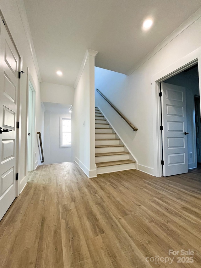 interior space featuring baseboards, stairway, wood finished floors, and crown molding