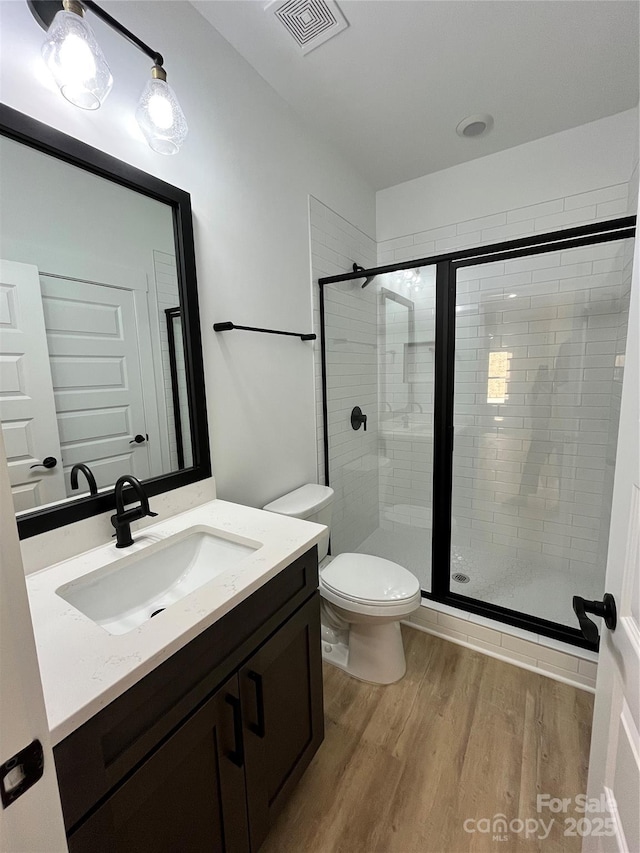 bathroom featuring a stall shower, visible vents, toilet, wood finished floors, and vanity