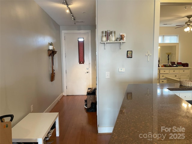 hallway featuring rail lighting, baseboards, and wood finished floors